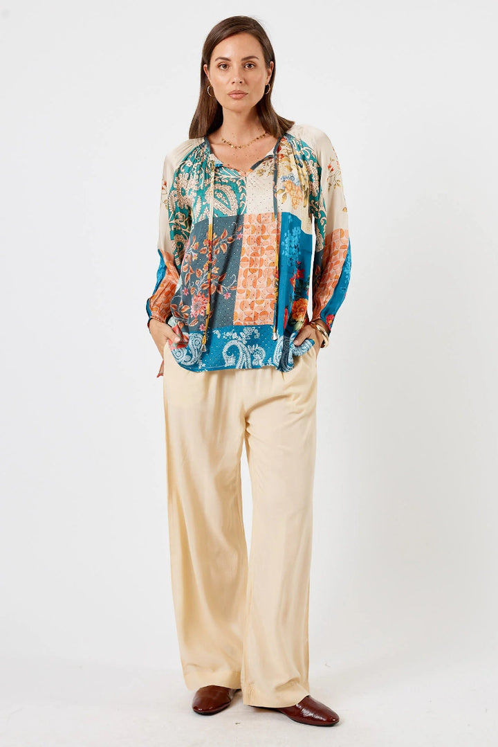 Woman wearing a colorful floral blouse and beige pants on a white background