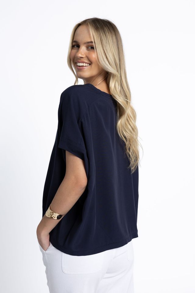 Woman wearing a navy blue top and white pants on a white background