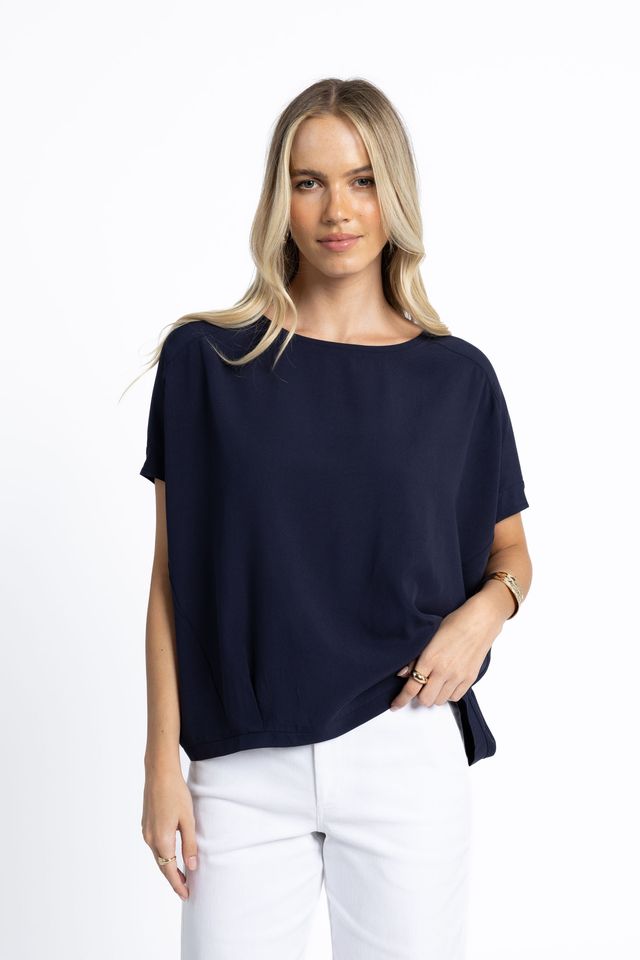 Woman wearing a navy blue top and white pants on a white background