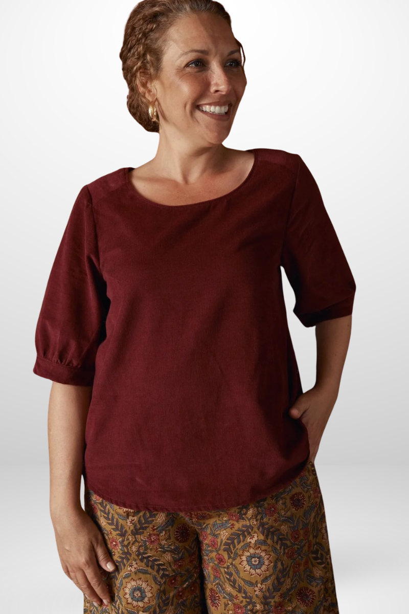 Woman wearing a burgundy top and patterned pants on a white background