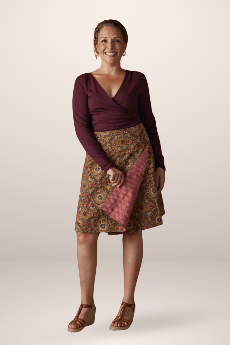 Woman wearing a patterned skirt and maroon top on a plain background
