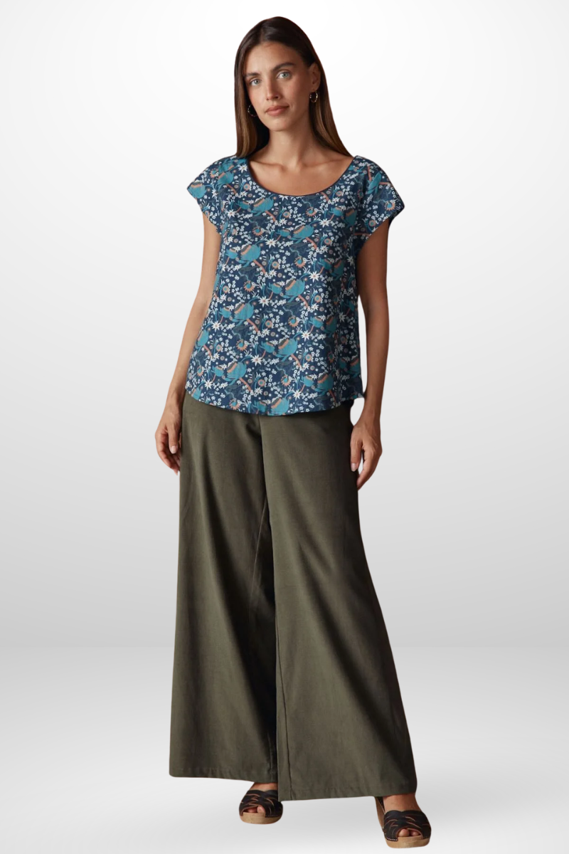 Woman wearing a blue floral top and green wide-leg pants on a white background