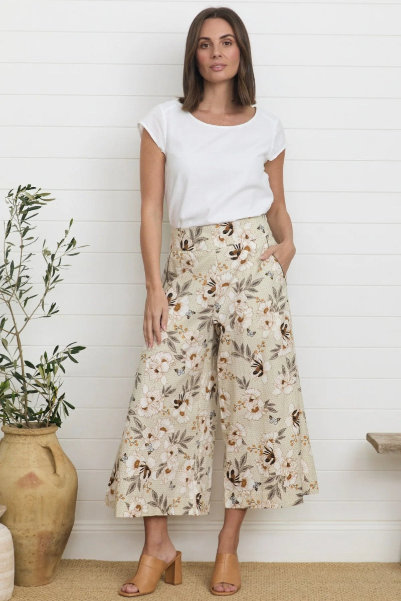 Woman wearing a white t-shirt and floral wide-leg pants standing against a white wall.