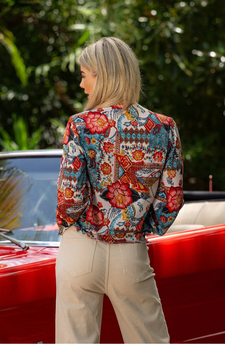 Back view of woman wearing patterned crossover blouse beside red car.