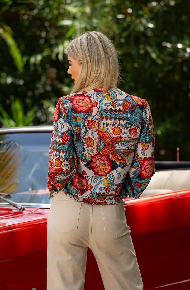 Back view of woman wearing patterned crossover blouse beside red car.