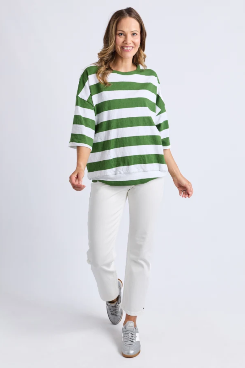Woman wearing a green and white striped shirt and white pants on a white background
