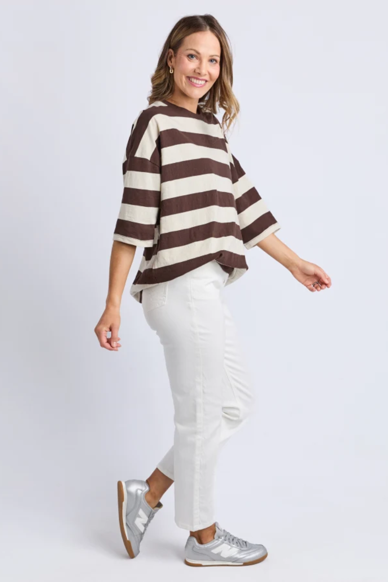 Woman wearing a brown and white striped sweater with white pants on a plain background
