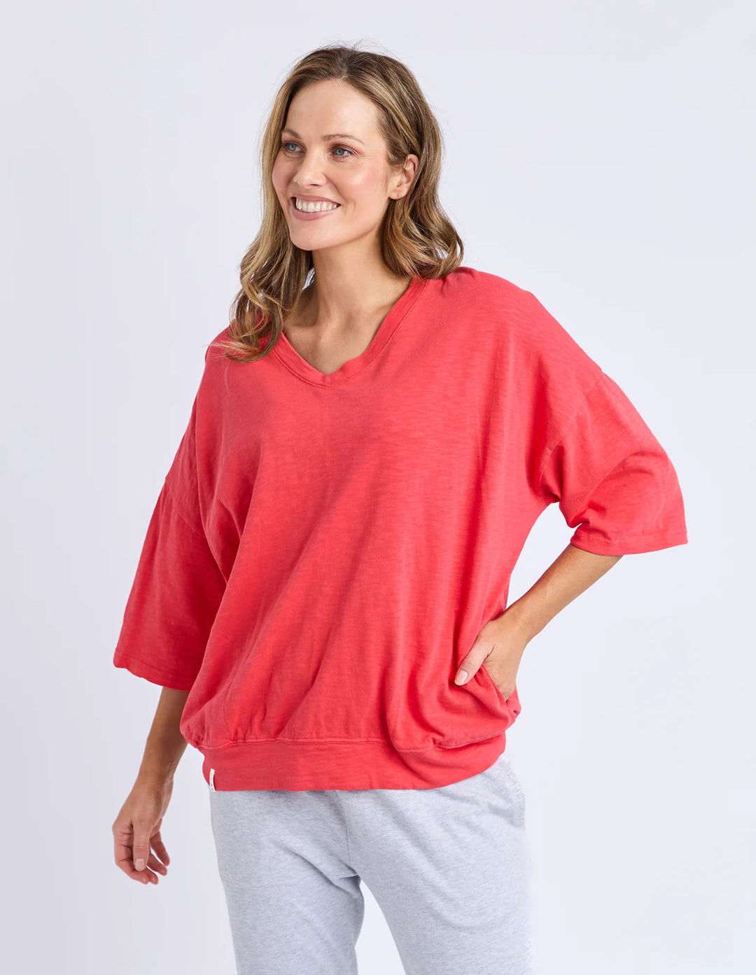 Woman wearing a red oversized sweater and gray pants on a white background