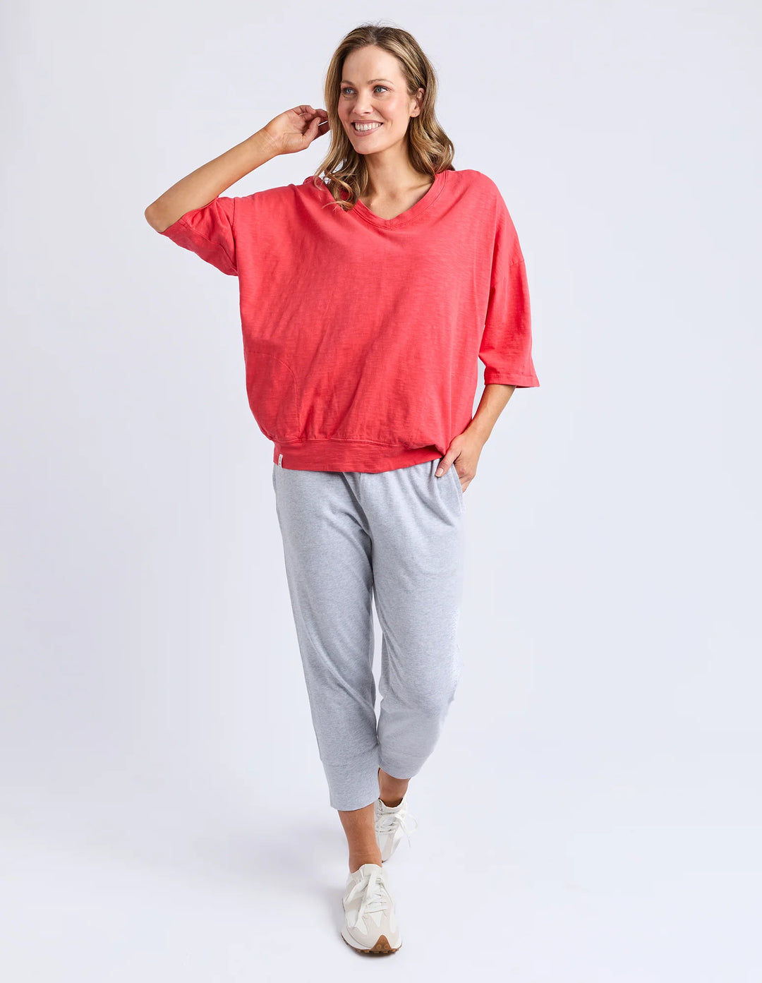Woman wearing a coral top and gray pants on a white background
