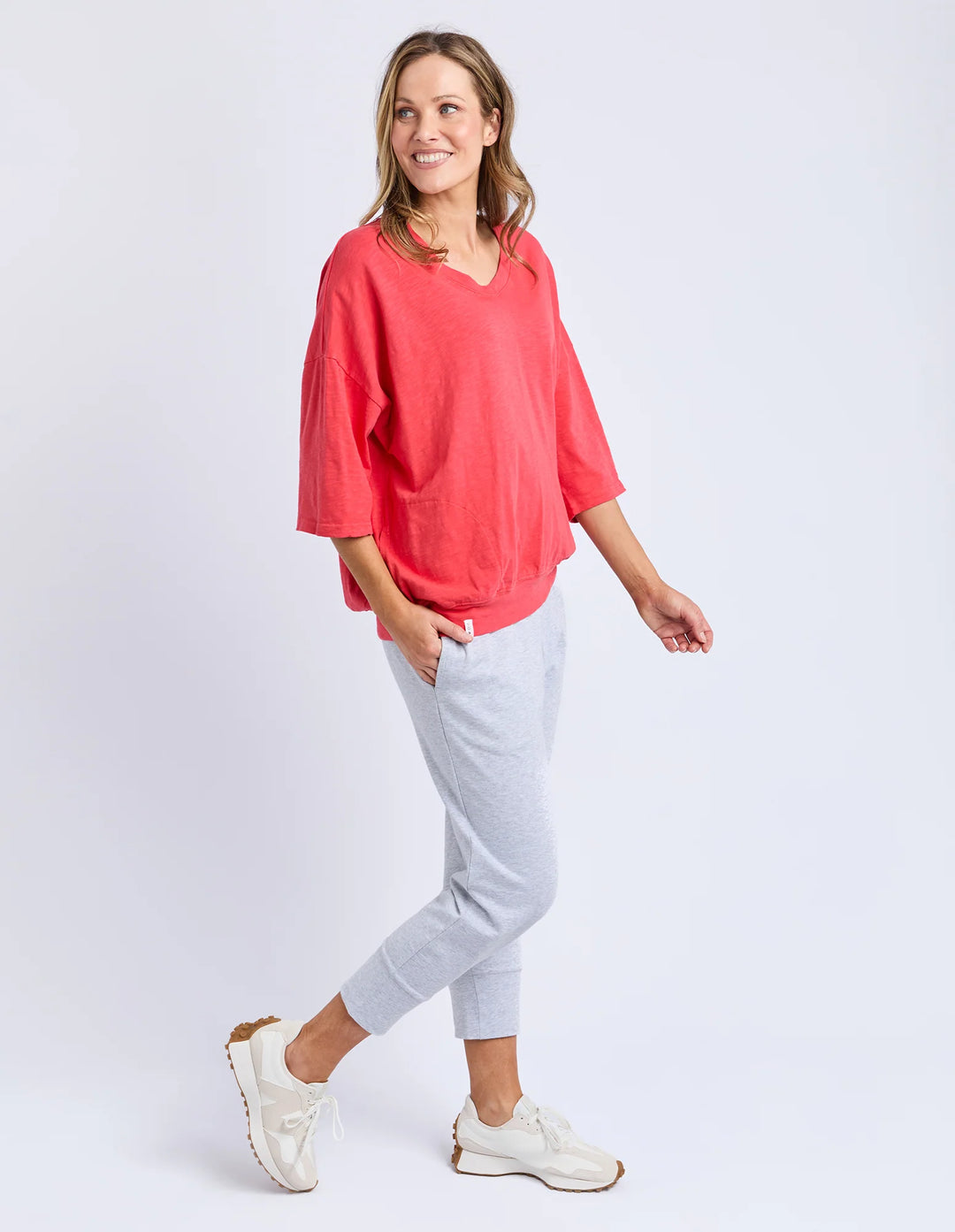 Woman wearing a coral top and gray pants on a white background