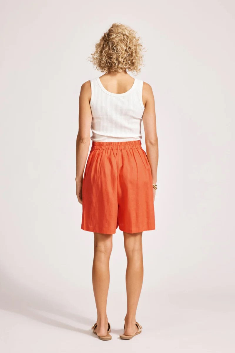 Person wearing a white tank top and orange shorts on a plain background