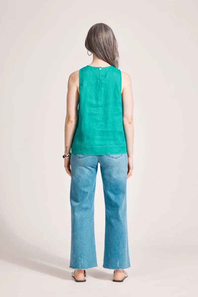 Person wearing a green sleeveless top and blue jeans on a plain background