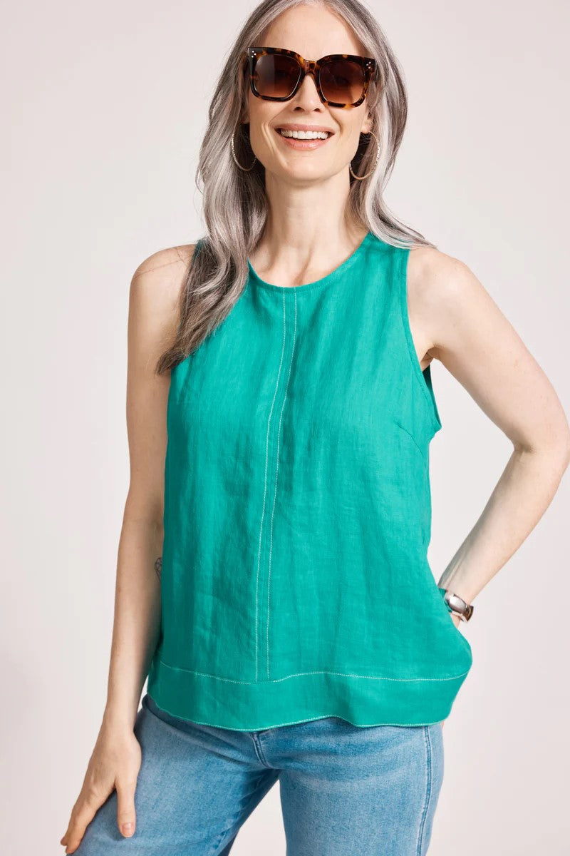 Woman wearing a green sleeveless top and sunglasses on a light pink background