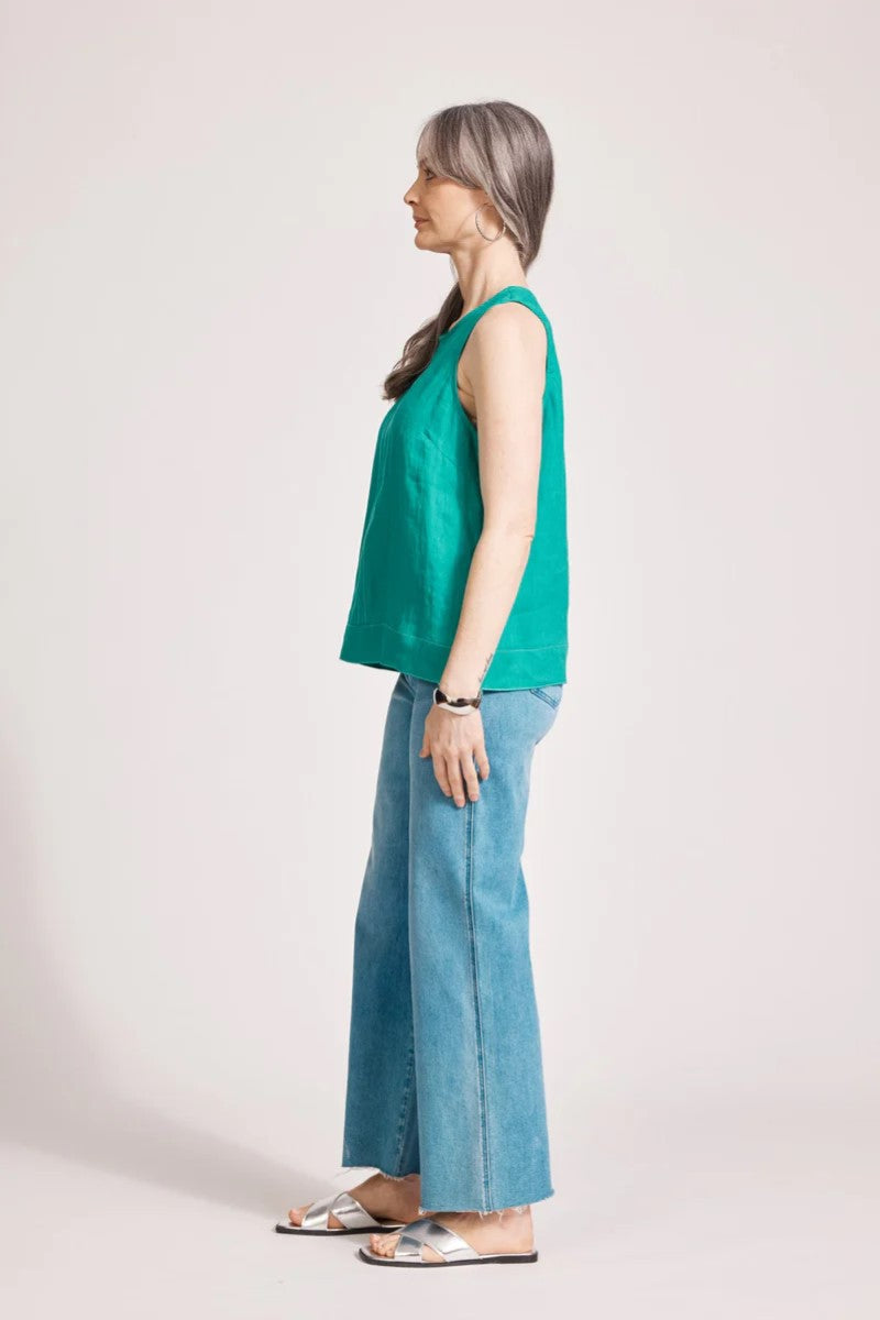 Woman wearing a green sleeveless top and blue jeans on a white background