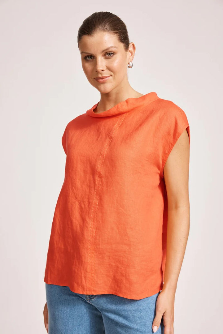 Woman wearing an orange sleeveless top and blue jeans on a light background