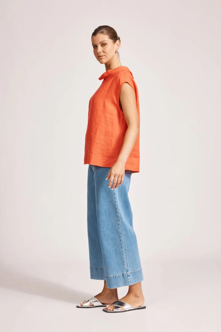 Woman wearing an orange sleeveless top and blue jeans on a light background