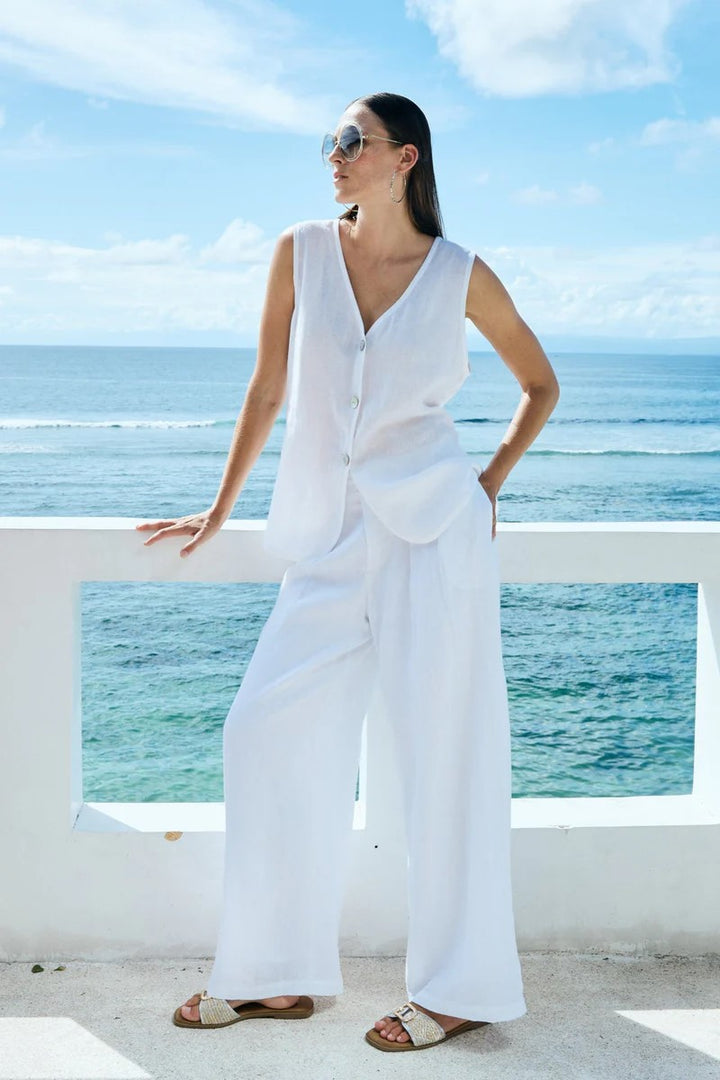 Woman in a white outfit standing by a railing with ocean view