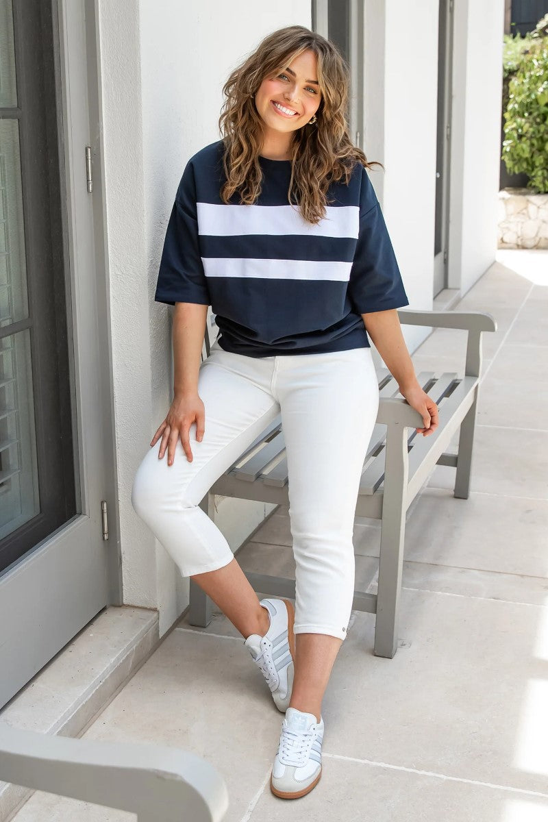 Woman wearing a navy and white striped shirt with white pants sitting on a bench.