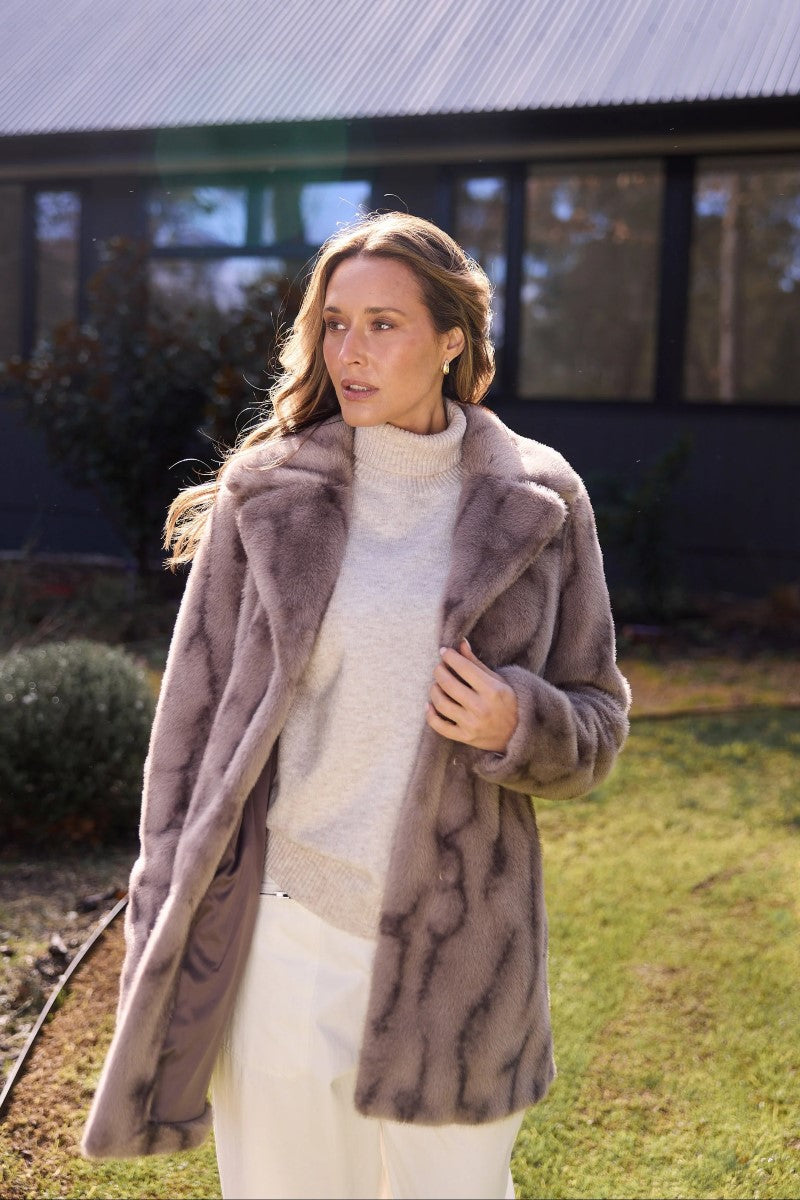 Lifestyle image of the Nadia Fur Coat in textured mink, styled with a lapel collar, fur hook closures, and mid-thigh length for a chic winter look.