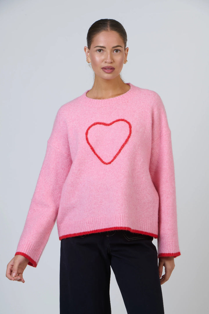 Woman wearing a pink sweater with a red heart design on a plain background