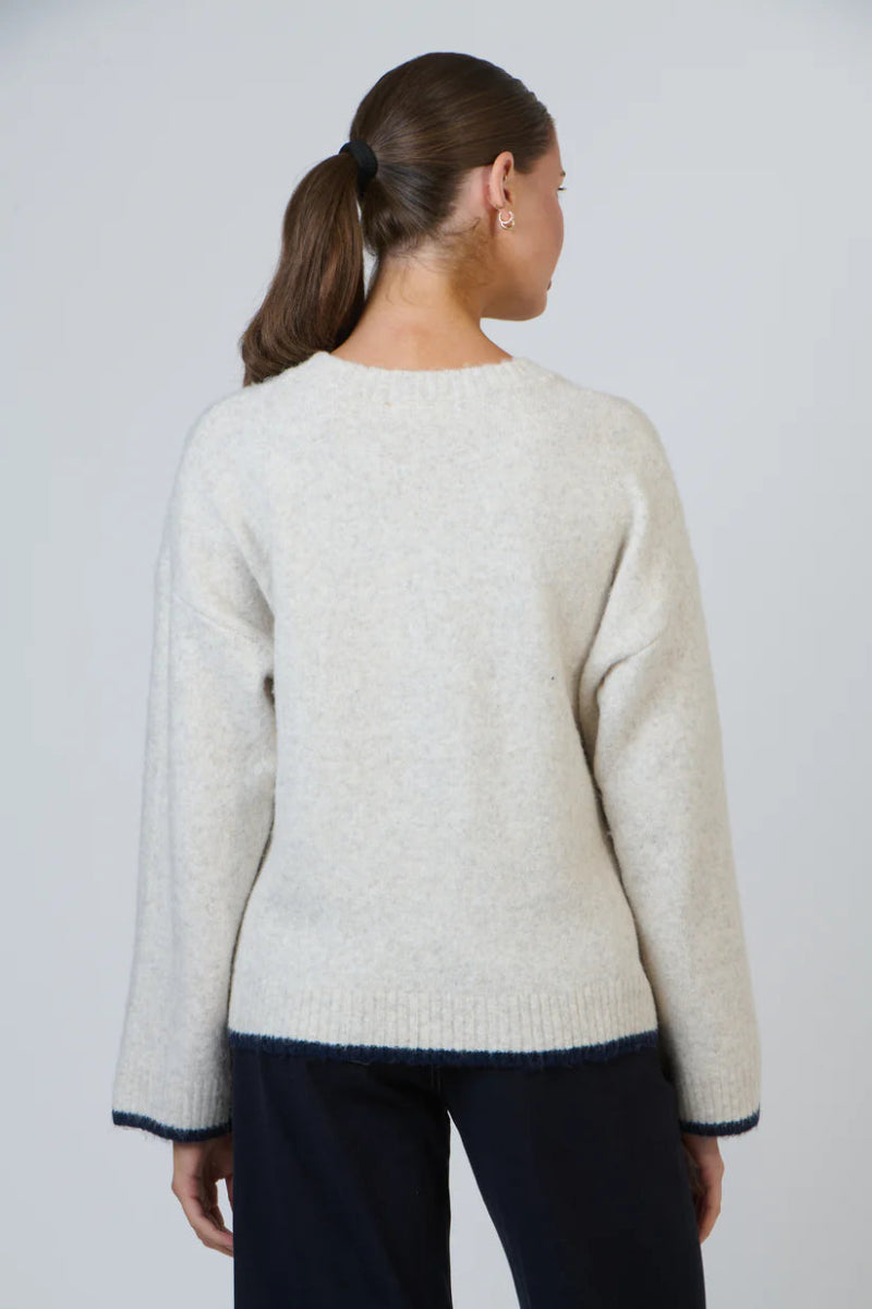 Woman wearing a light gray sweater with dark blue trim on a plain background