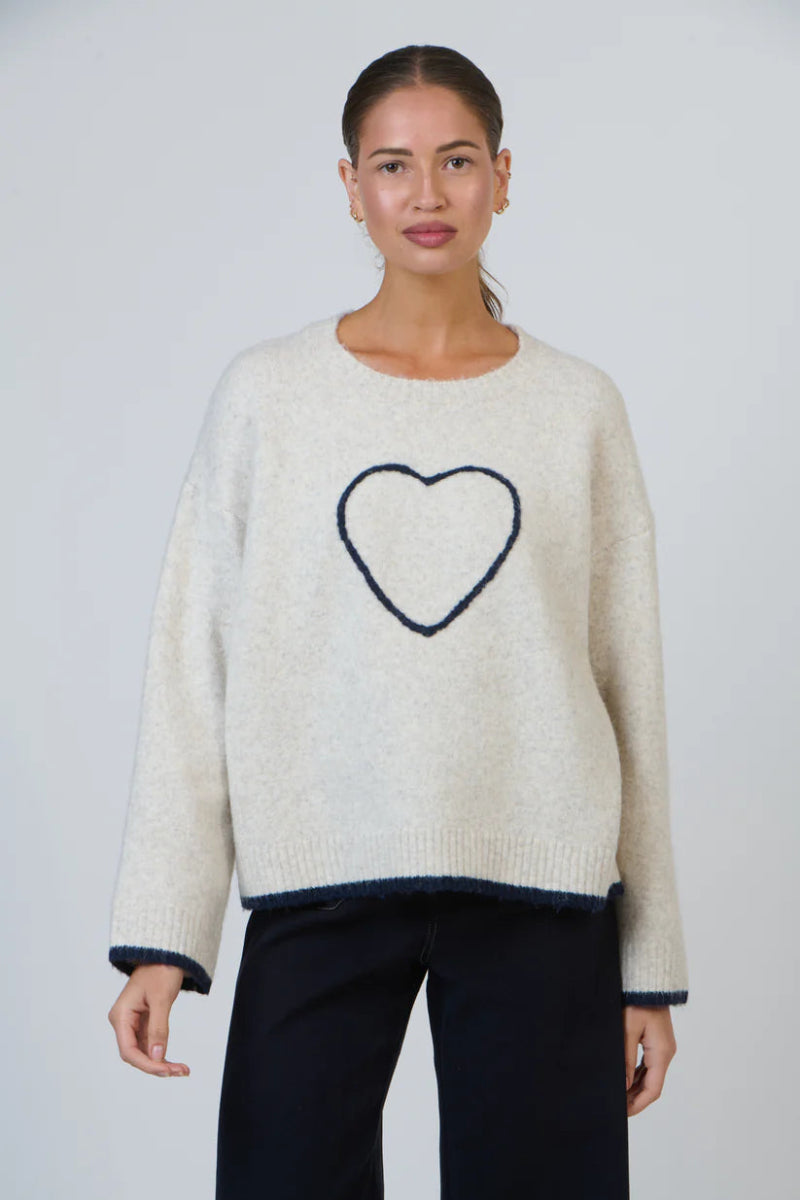 Woman wearing a cream sweater with a heart design on a plain background