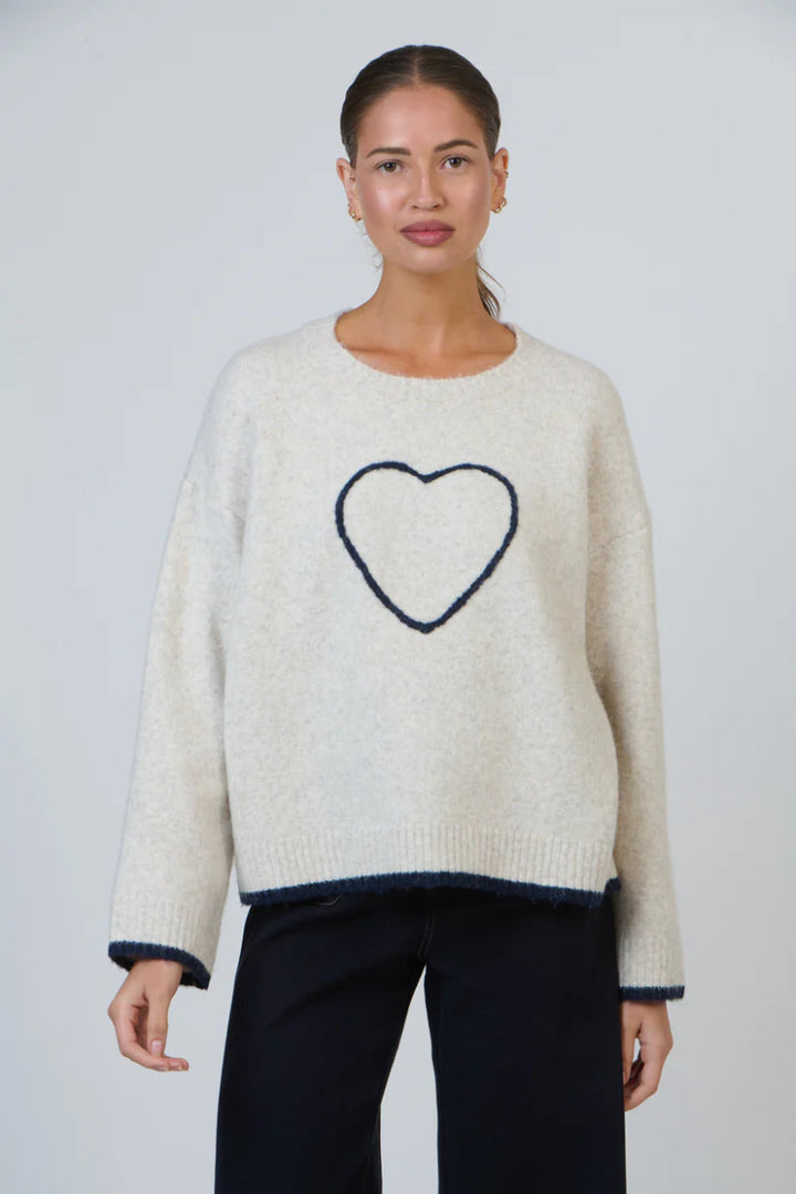 Woman wearing a cream sweater with a heart design on a plain background