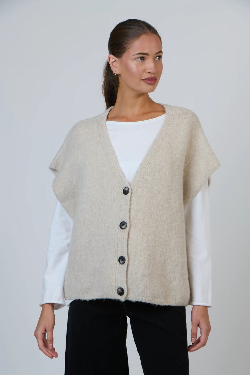Woman wearing a beige cardigan over a white shirt on a plain background