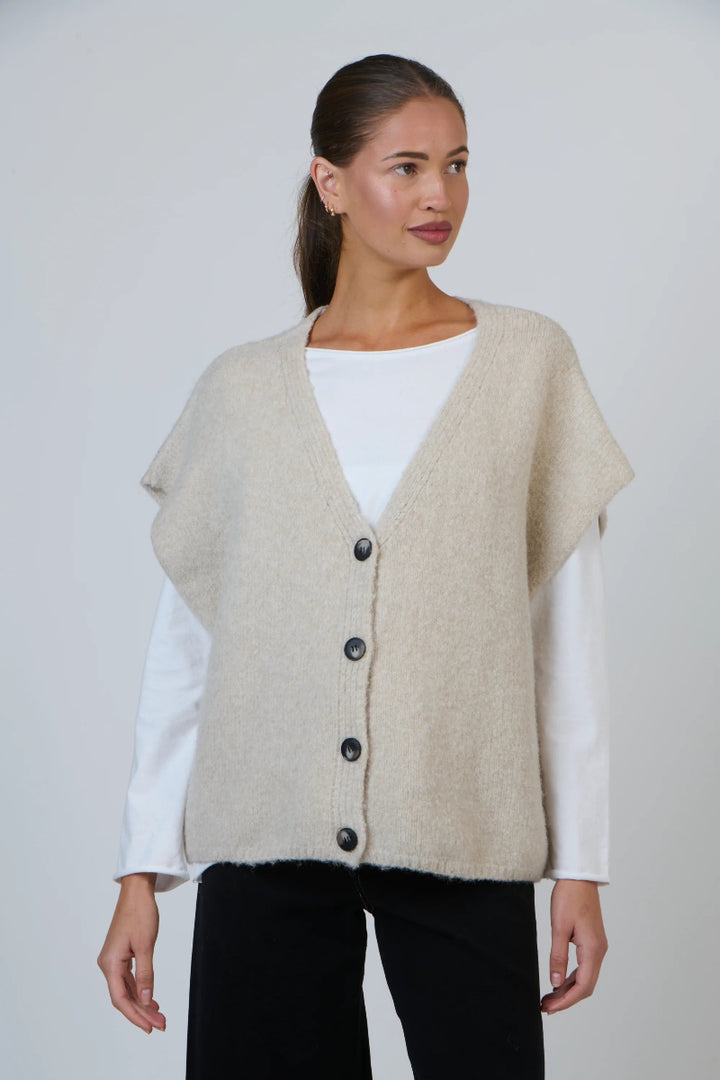 Woman wearing a beige cardigan over a white shirt on a plain background