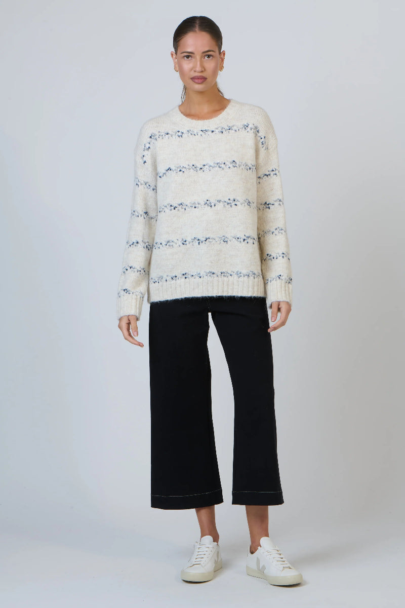 Woman wearing a patterned sweater and black pants on a white background