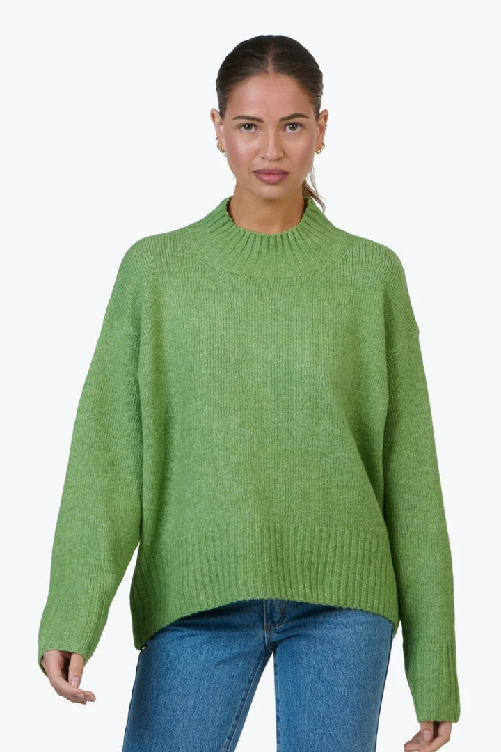 Woman wearing a green sweater and blue jeans on a white background
