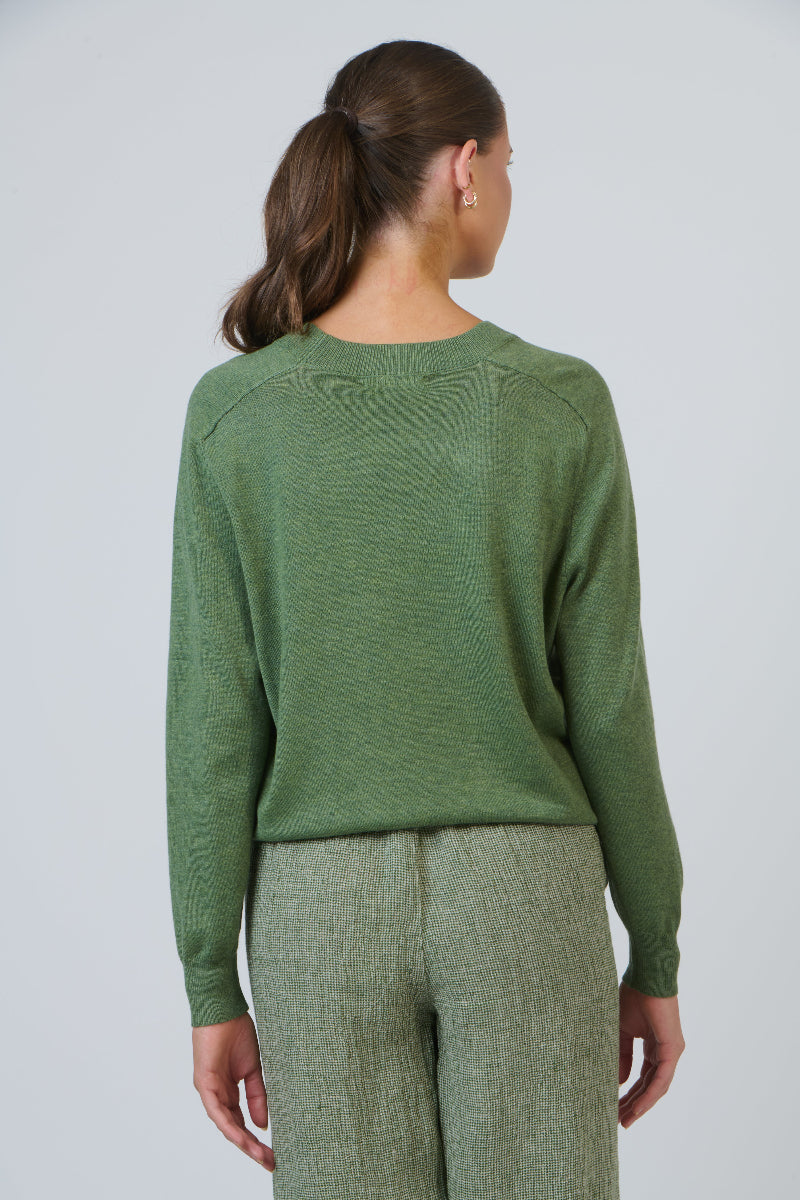 Person wearing a green sweater and pants against a plain background