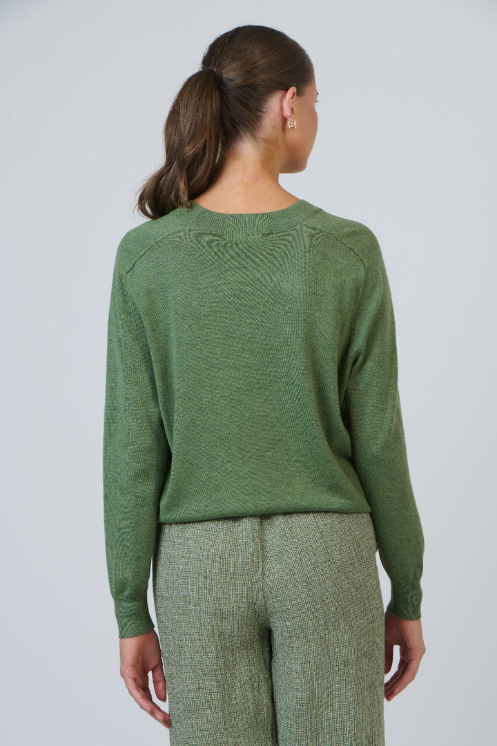 Person wearing a green sweater and pants against a plain background