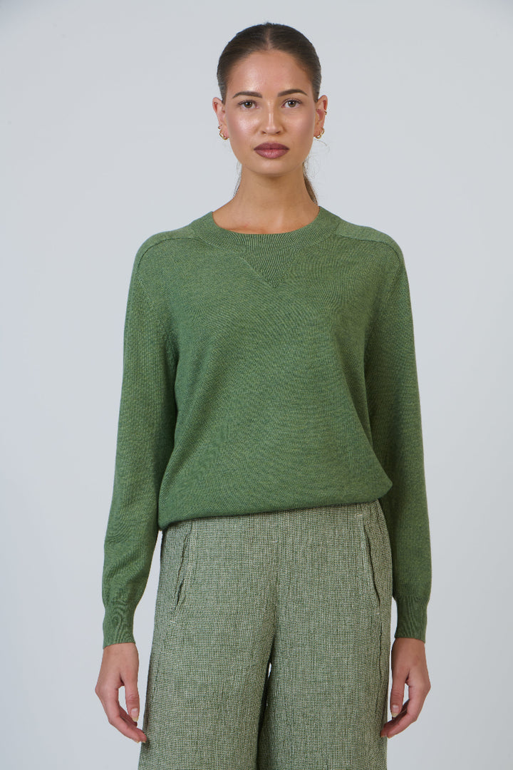 Woman wearing a green sweater and pants against a white background