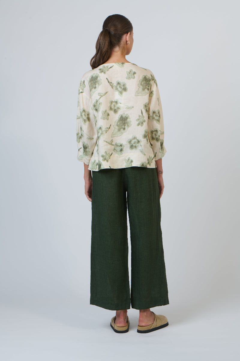 Person wearing a floral blouse and green pants on a white background