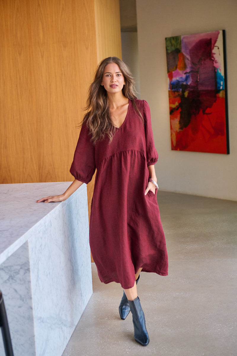 Woman in a burgundy dress standing in a modern interior setting with abstract art on the wall.
