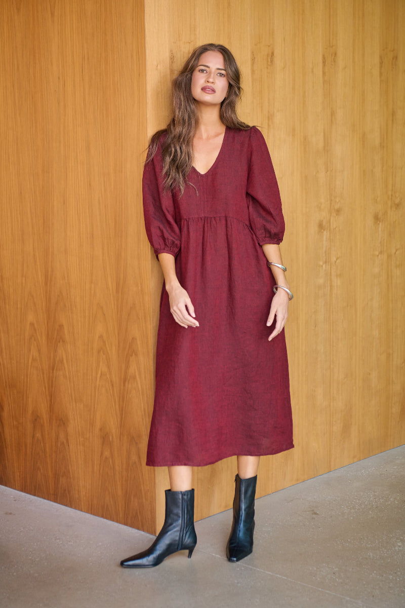 Woman wearing a burgundy dress with puffed sleeves against a wooden wall.