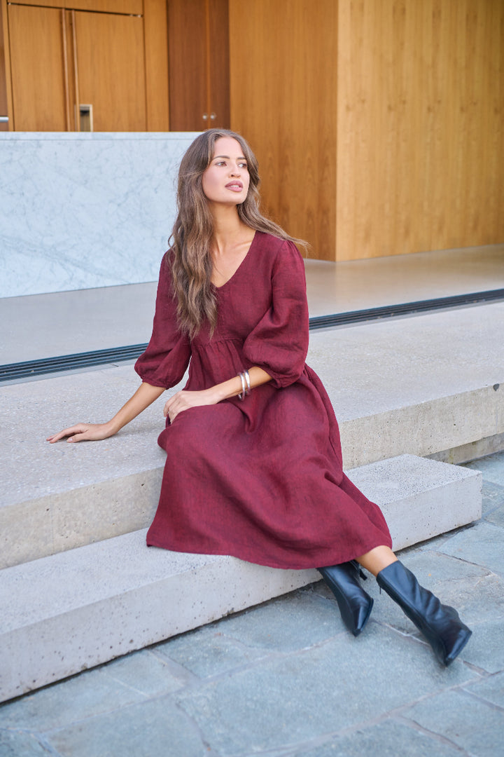 Woman in a burgundy dress sitting on stone steps with wooden walls in the background