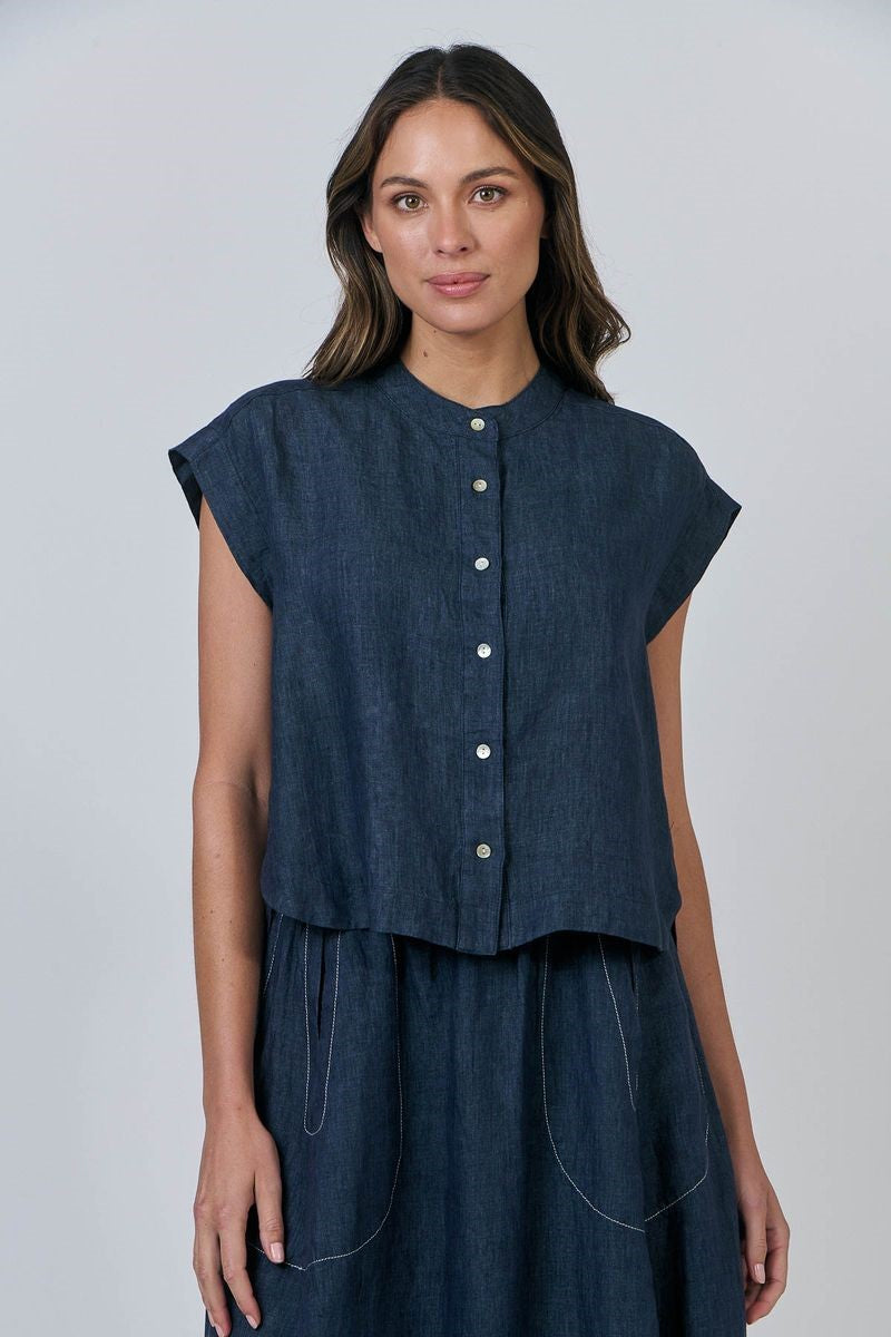 Woman wearing a dark blue sleeveless top with buttons on a plain background