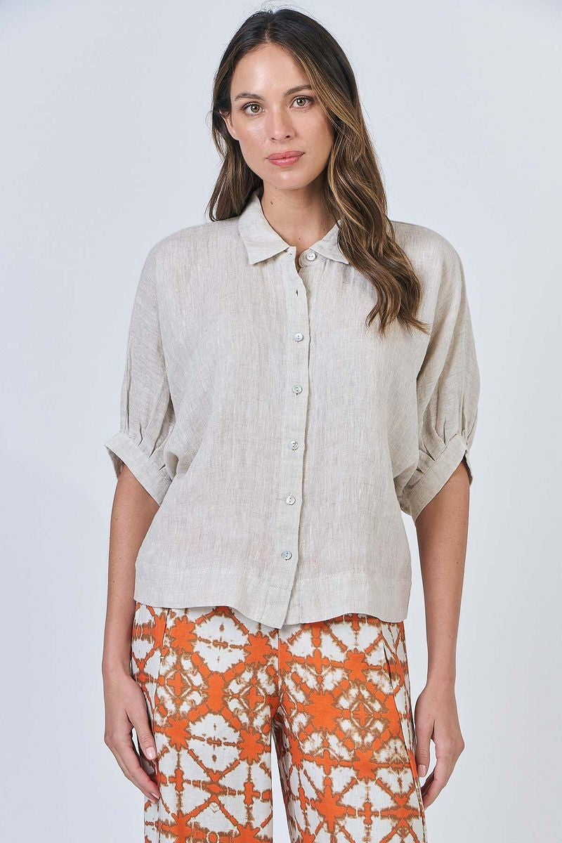 Woman wearing a beige button-up shirt and orange floral pants on a white background
