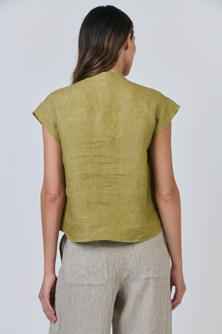 Woman wearing a green sleeveless top and beige pants against a white background