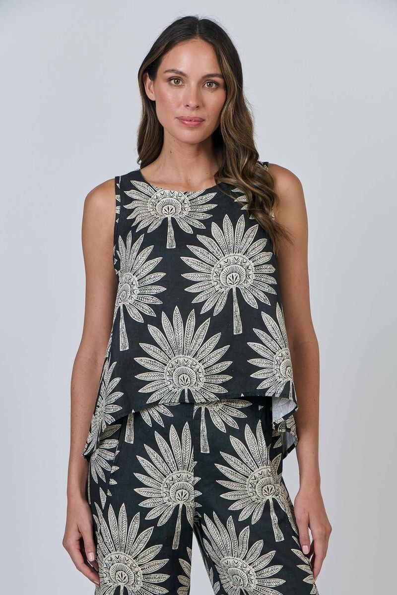 Woman wearing a black sleeveless top and pants with white floral patterns on a plain background