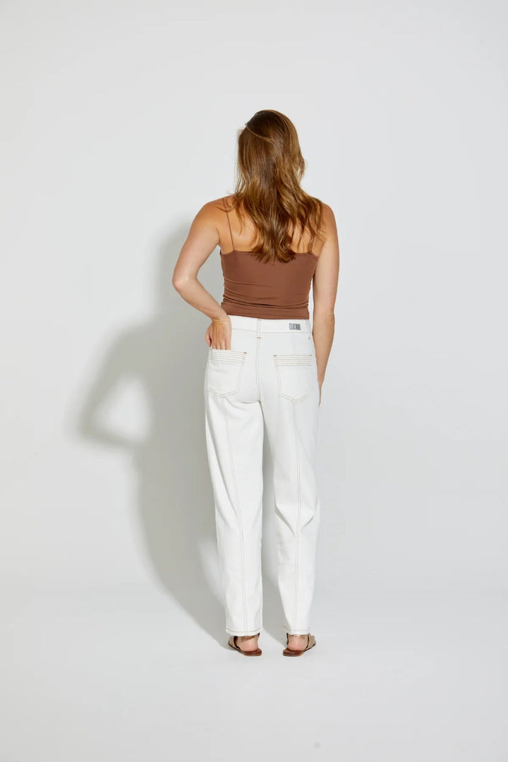 Woman wearing a brown top and white pants on a plain background