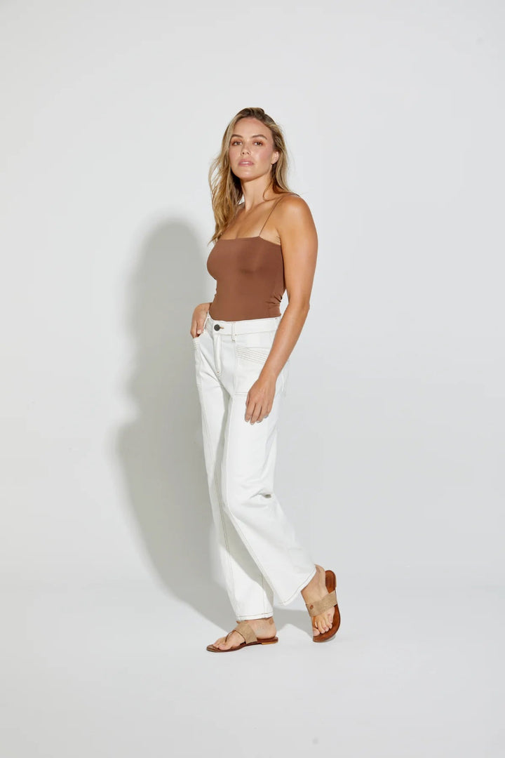 Woman wearing a brown top and white pants against a plain background