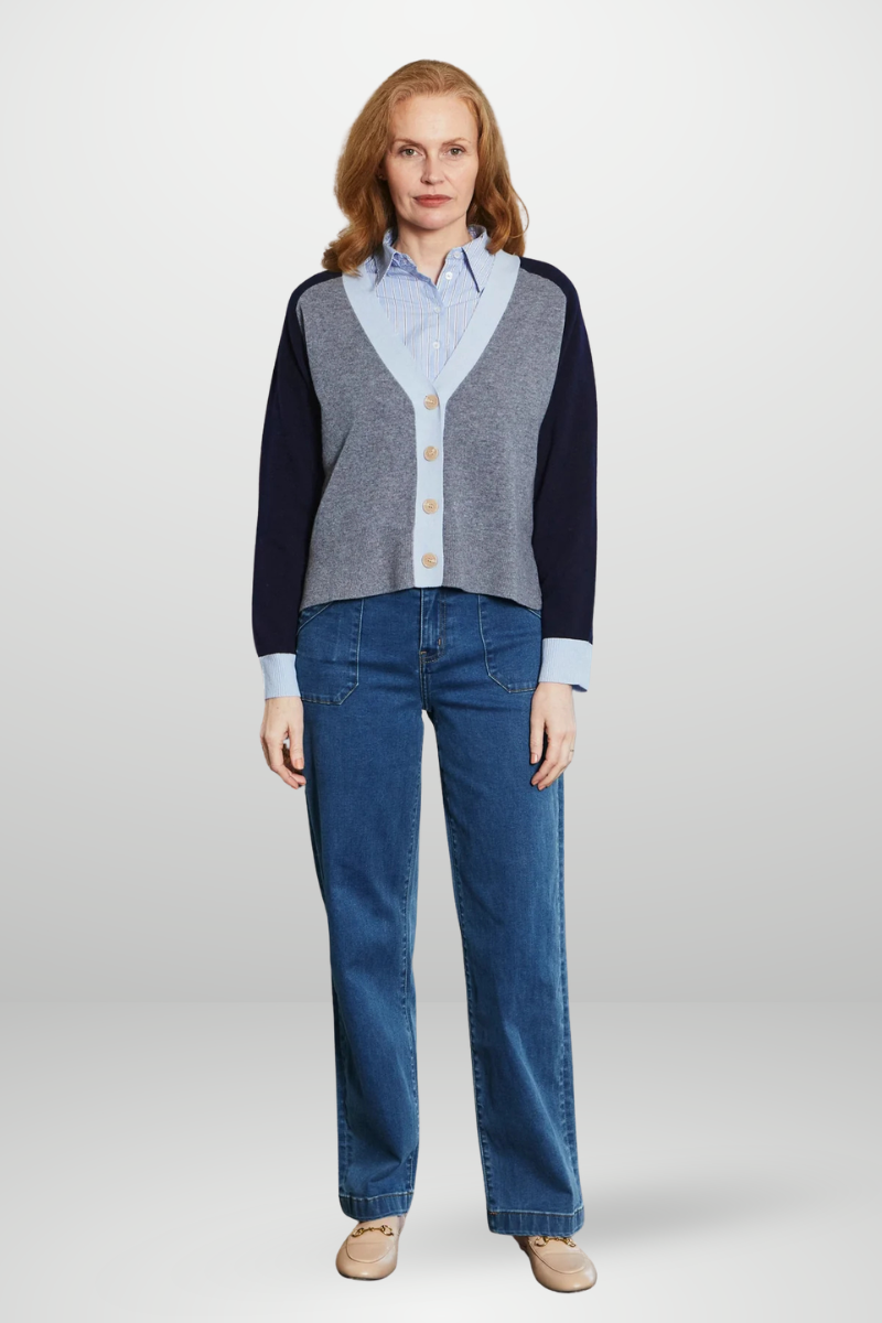 Woman wearing a navy cardigan, light blue shirt, and jeans on a white background