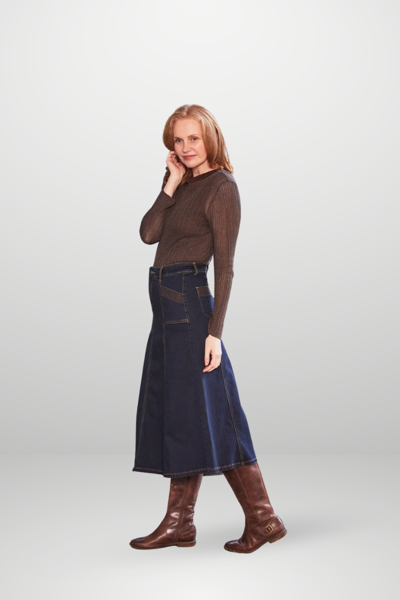 Woman wearing a brown mesh top and blue denim skirt with brown boots on a white background