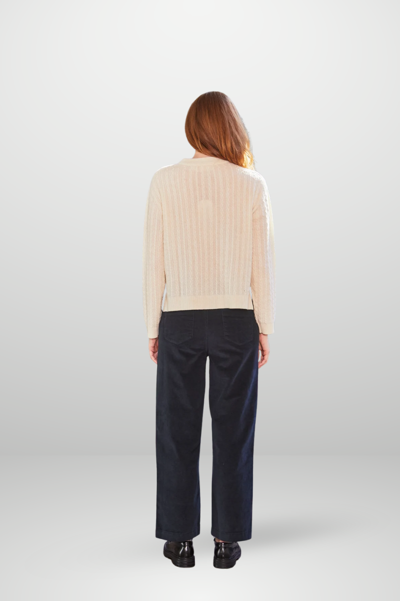 Person wearing a beige sweater and dark pants on a white background