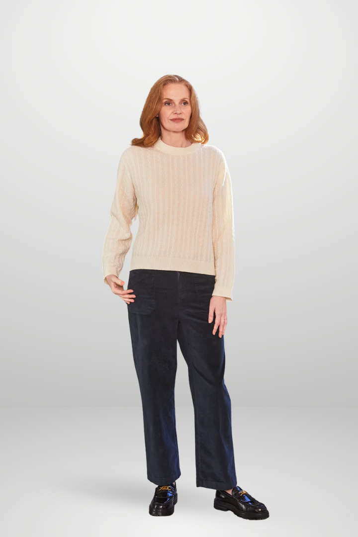 Woman wearing a beige sweater and dark pants on a white background