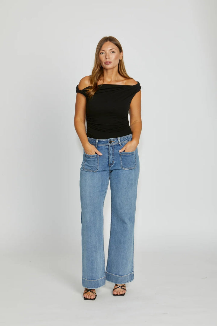 Woman wearing a black off-shoulder top and blue jeans on a white background