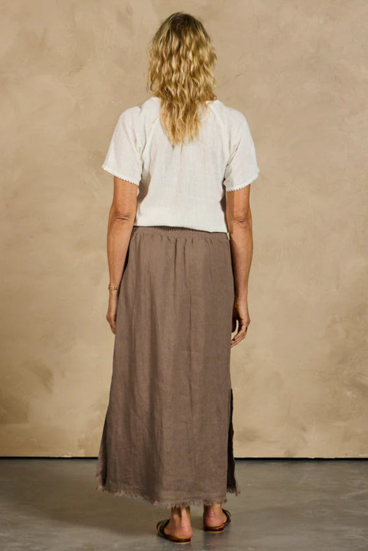 Person wearing a white top and brown skirt against a beige wall.